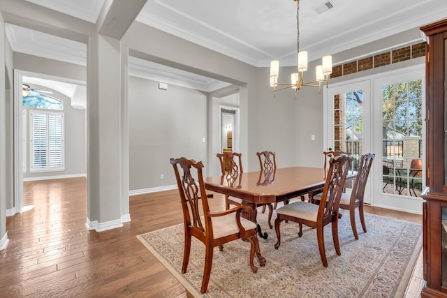 dining area featuring baseboards, visible vents, wood-type flooring, crown molding, and a notable chandelier