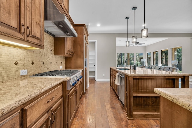 kitchen with light stone counters, stainless steel appliances, a sink, under cabinet range hood, and backsplash