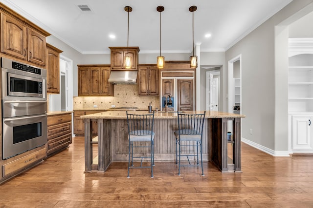 kitchen featuring light stone countertops, visible vents, paneled built in fridge, a kitchen bar, and wall chimney range hood