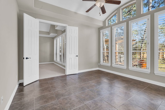 empty room featuring lofted ceiling, dark tile patterned floors, baseboards, and ceiling fan