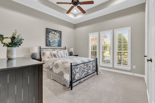 bedroom with a raised ceiling, light colored carpet, baseboards, and ceiling fan