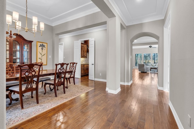 dining space with ornamental molding, arched walkways, dark wood-style flooring, and baseboards