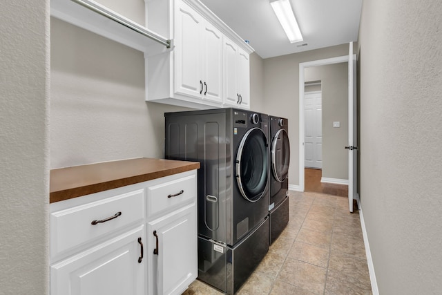 laundry area featuring washing machine and clothes dryer, cabinet space, baseboards, and a textured wall