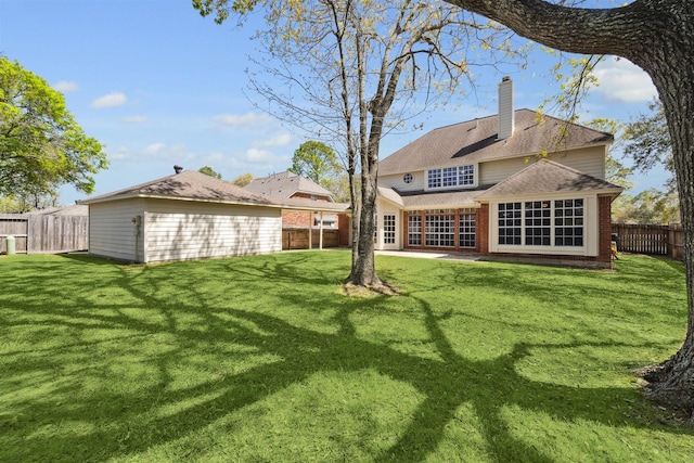 back of house with brick siding, a shingled roof, a lawn, a chimney, and a fenced backyard