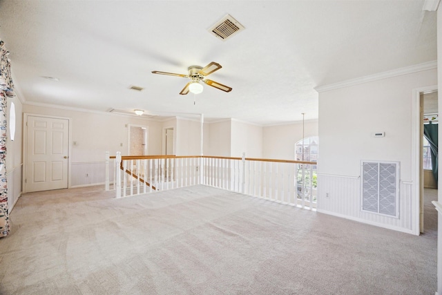 carpeted empty room with a wainscoted wall, crown molding, visible vents, and ceiling fan