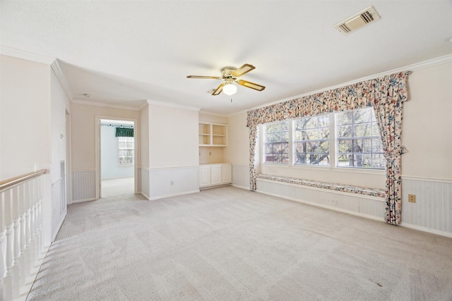 empty room with a ceiling fan, a healthy amount of sunlight, visible vents, and wainscoting