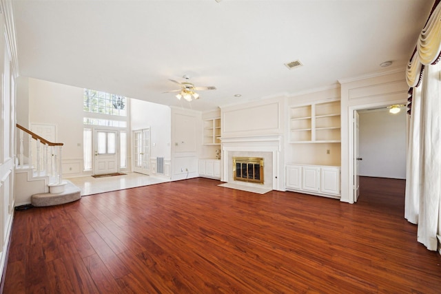 unfurnished living room with visible vents, built in shelves, ceiling fan, stairway, and dark wood-style floors