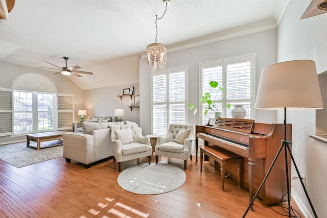 living area featuring a healthy amount of sunlight, ceiling fan with notable chandelier, lofted ceiling, and wood finished floors