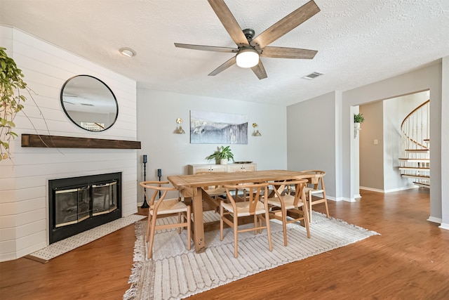 dining space with visible vents, wood finished floors, stairway, a fireplace, and ceiling fan