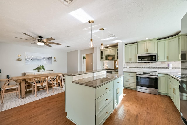 kitchen featuring light wood finished floors, stone counters, appliances with stainless steel finishes, and green cabinetry