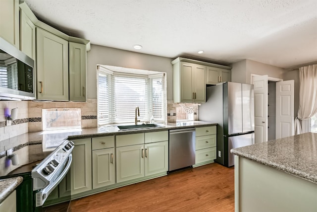 kitchen with green cabinetry, light wood-style flooring, appliances with stainless steel finishes, and a sink