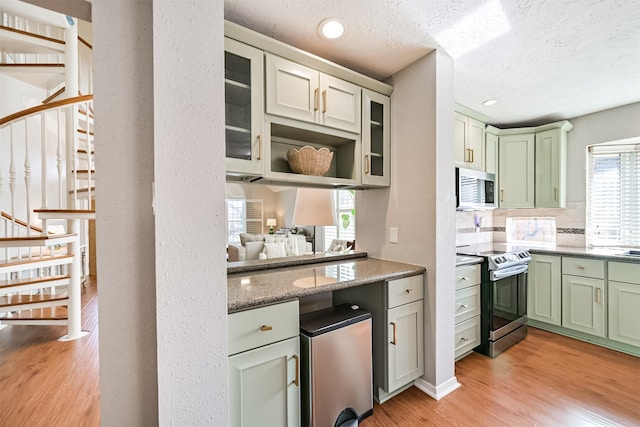 kitchen featuring light wood-style flooring, glass insert cabinets, appliances with stainless steel finishes, green cabinets, and tasteful backsplash