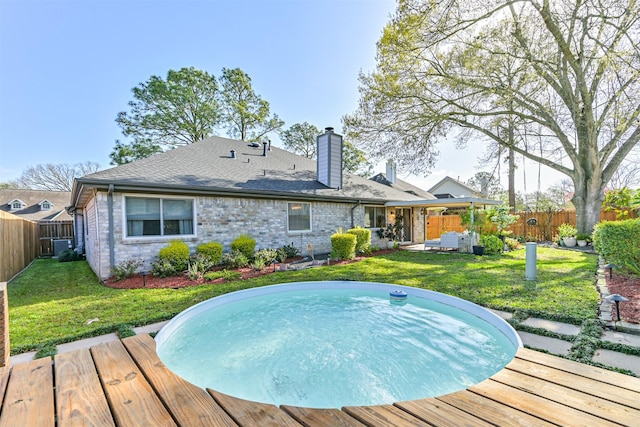 rear view of house with brick siding, a fenced backyard, a chimney, and a yard