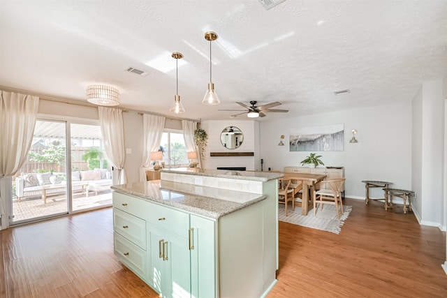 kitchen featuring visible vents, a center island, ceiling fan, decorative light fixtures, and light wood-style floors