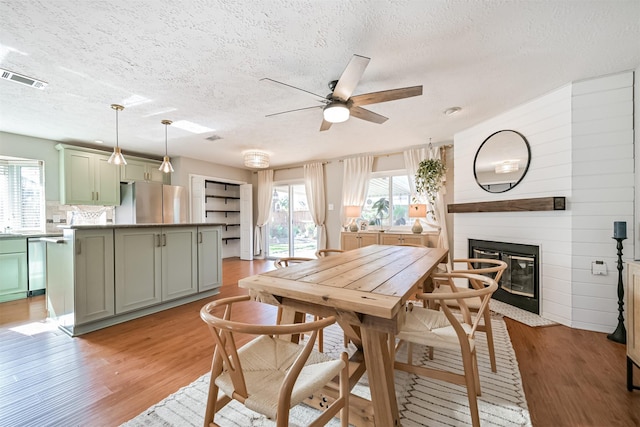 dining room with visible vents, light wood-style flooring, ceiling fan, a textured ceiling, and a large fireplace