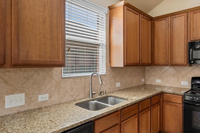 kitchen featuring light stone counters, brown cabinetry, a sink, decorative backsplash, and black appliances