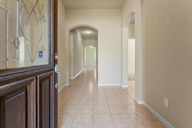 interior space with baseboards, arched walkways, and light tile patterned flooring