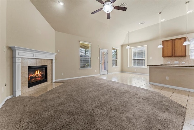 unfurnished living room featuring a tiled fireplace, light colored carpet, vaulted ceiling, light tile patterned floors, and a ceiling fan