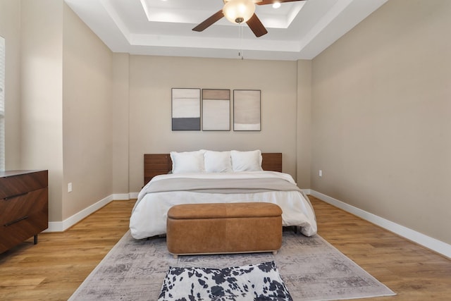 bedroom featuring a ceiling fan, a tray ceiling, light wood-style floors, and baseboards