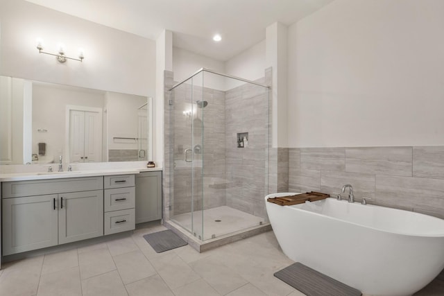 full bathroom with tile walls, a shower stall, tile patterned flooring, a freestanding bath, and vanity