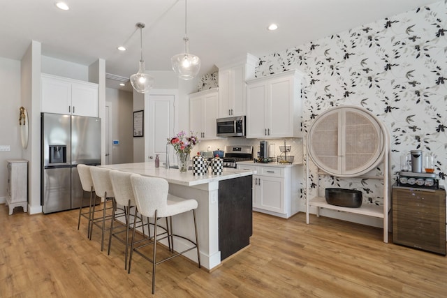 kitchen with white cabinets, light wood-style flooring, a kitchen breakfast bar, and stainless steel appliances