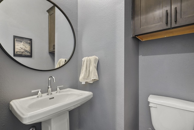 bathroom featuring toilet, a textured wall, and a sink