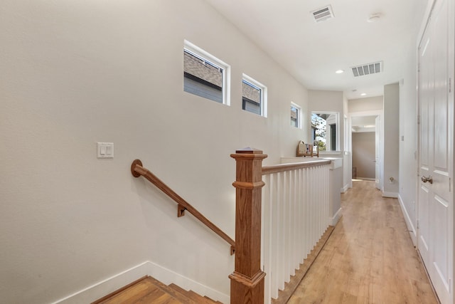 hallway with visible vents, an upstairs landing, baseboards, and light wood finished floors