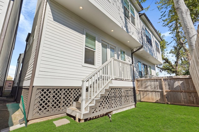 rear view of house featuring a lawn, stairs, and fence