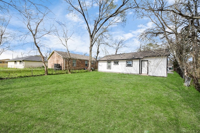 rear view of house featuring an outbuilding, a yard, and fence