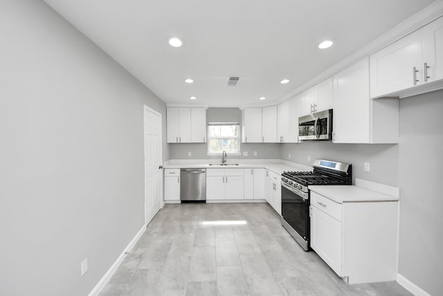 kitchen with baseboards, light countertops, stainless steel appliances, white cabinetry, and a sink