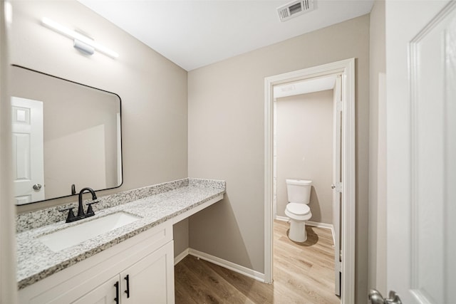 bathroom with vanity, wood finished floors, visible vents, baseboards, and toilet