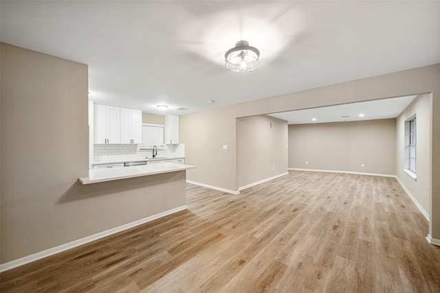 unfurnished living room with light wood-style floors, baseboards, and a sink