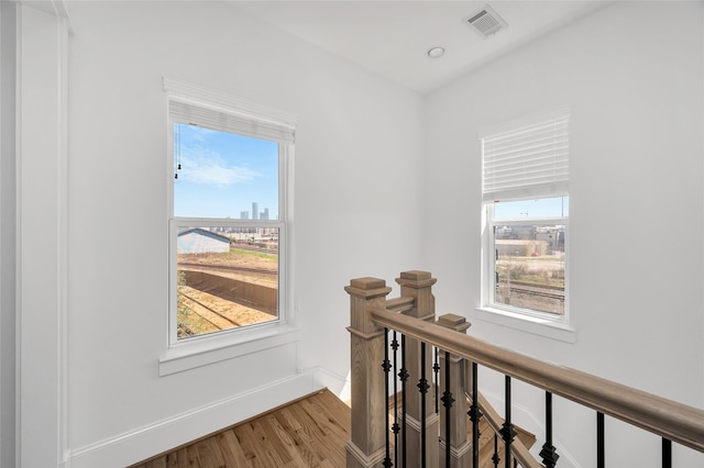 hallway featuring visible vents, an upstairs landing, a view of city, wood finished floors, and baseboards