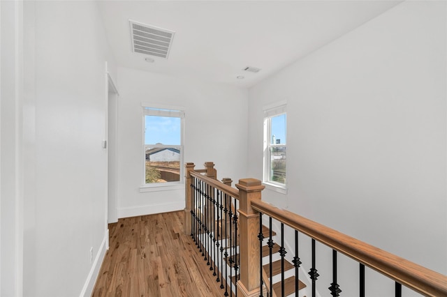 hall with an upstairs landing, visible vents, a healthy amount of sunlight, and light wood-style flooring