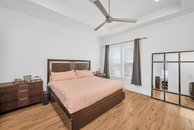 bedroom featuring baseboards, light wood-type flooring, a tray ceiling, and a ceiling fan