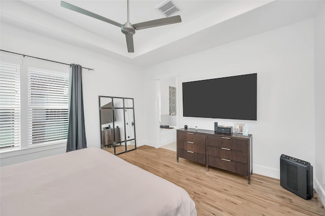 bedroom featuring visible vents, light wood-style flooring, a raised ceiling, and baseboards