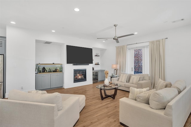 living area featuring ceiling fan, visible vents, light wood-style floors, and a glass covered fireplace