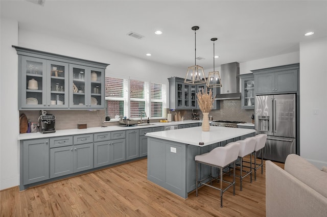 kitchen featuring wall chimney range hood, gray cabinets, visible vents, and high end fridge