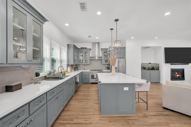 kitchen featuring visible vents, gray cabinetry, stainless steel appliances, wall chimney exhaust hood, and a sink