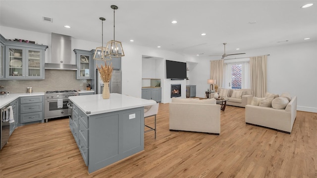 kitchen featuring gray cabinets, stainless steel range, light countertops, light wood-style floors, and wall chimney range hood