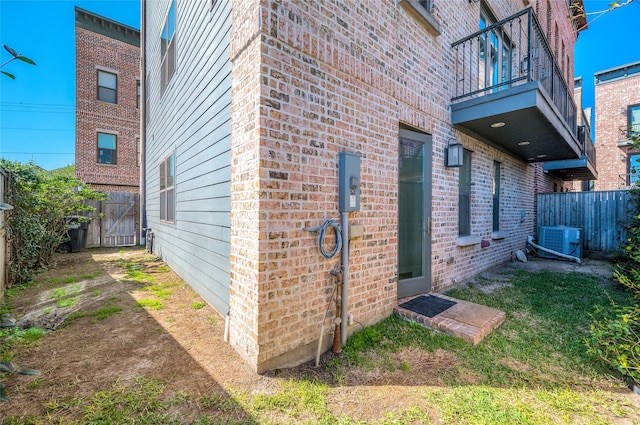 view of property exterior featuring a balcony, central air condition unit, a fenced backyard, and brick siding