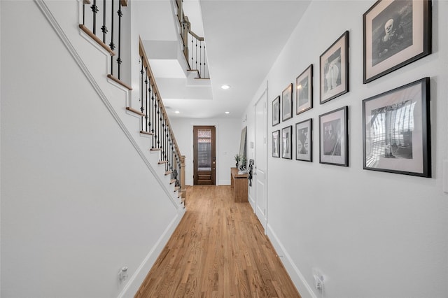 corridor with light wood finished floors, stairway, recessed lighting, and baseboards