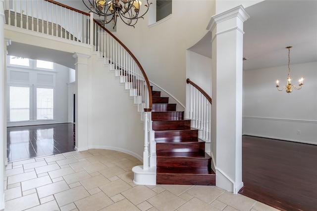 stairway featuring a notable chandelier, wood finished floors, baseboards, a towering ceiling, and ornate columns