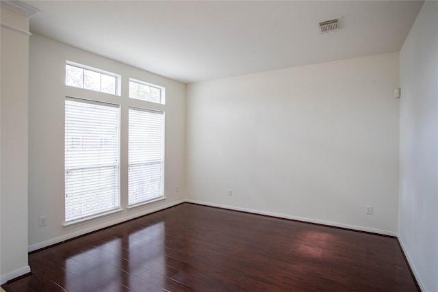 empty room featuring visible vents, baseboards, and dark wood-type flooring