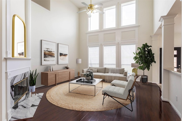 living area with wood finished floors, baseboards, a premium fireplace, ceiling fan, and a towering ceiling