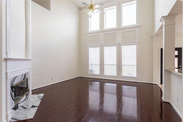 unfurnished living room featuring ceiling fan, wood finished floors, a fireplace, baseboards, and a towering ceiling