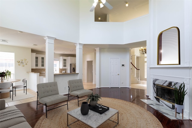 living room featuring a fireplace with flush hearth, stairway, decorative columns, wood finished floors, and a ceiling fan