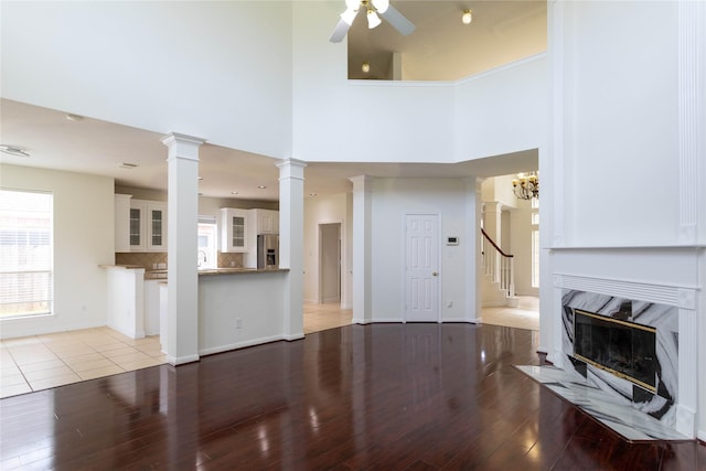 living area with a ceiling fan, wood finished floors, a high end fireplace, baseboards, and ornate columns