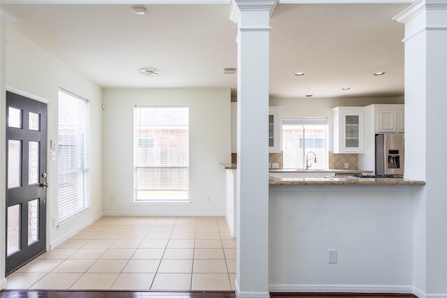 kitchen featuring light tile patterned flooring, a sink, white cabinets, glass insert cabinets, and stainless steel refrigerator with ice dispenser