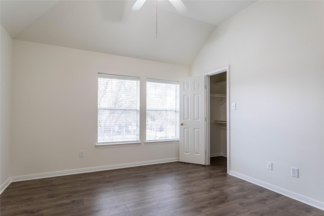 unfurnished bedroom featuring a walk in closet, vaulted ceiling, baseboards, and dark wood-type flooring